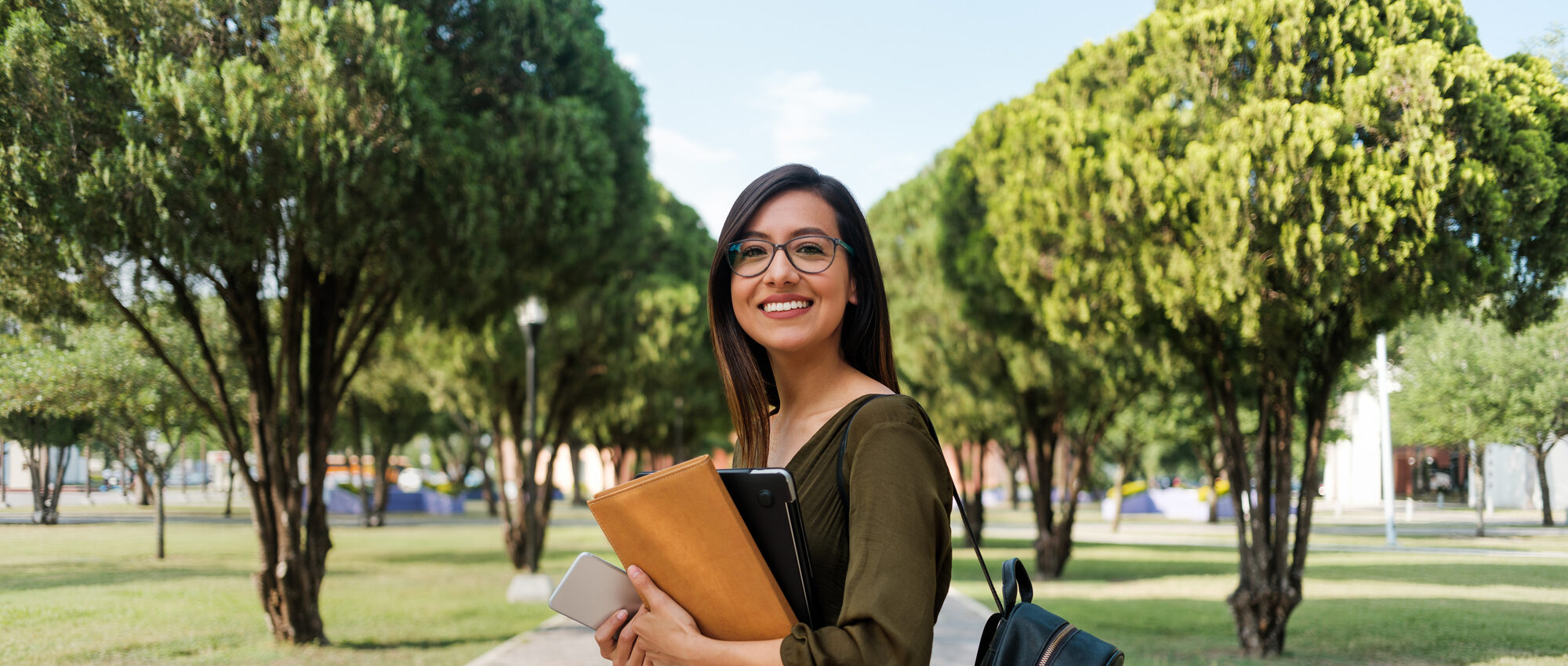 College student with long hair and glasses smiling while holding a tablet.